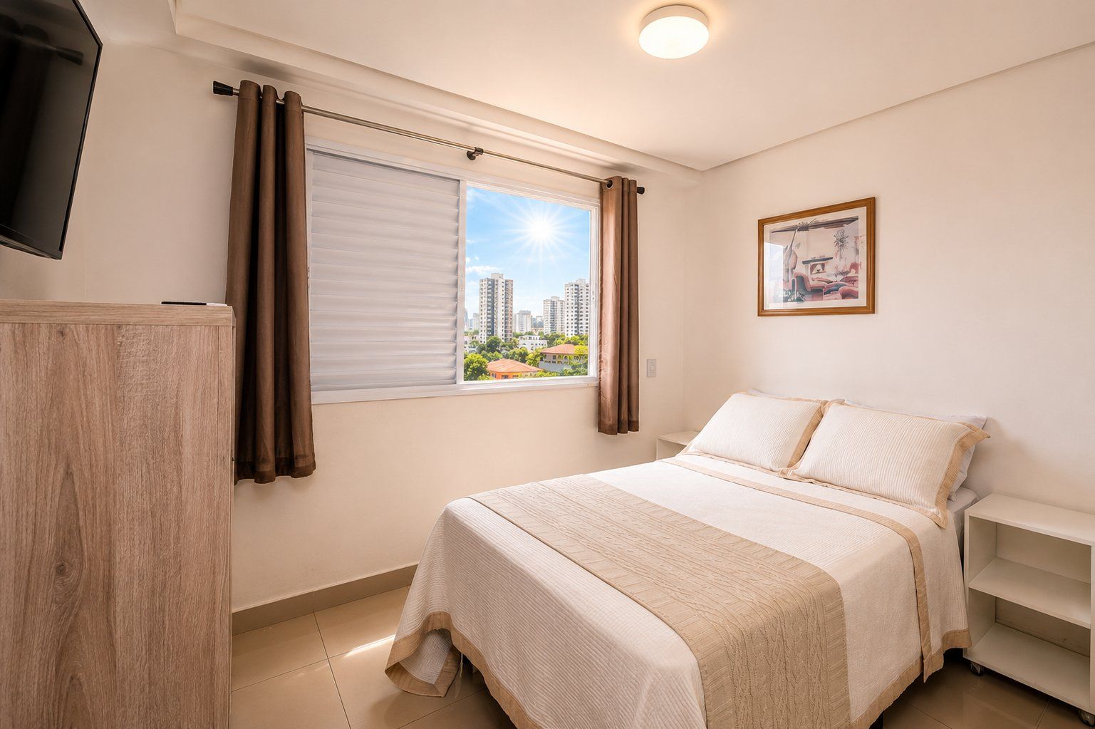 Un dormitorio con cama, televisor, ventana con cortinas, un cuadro en la pared y vistas de edificios.