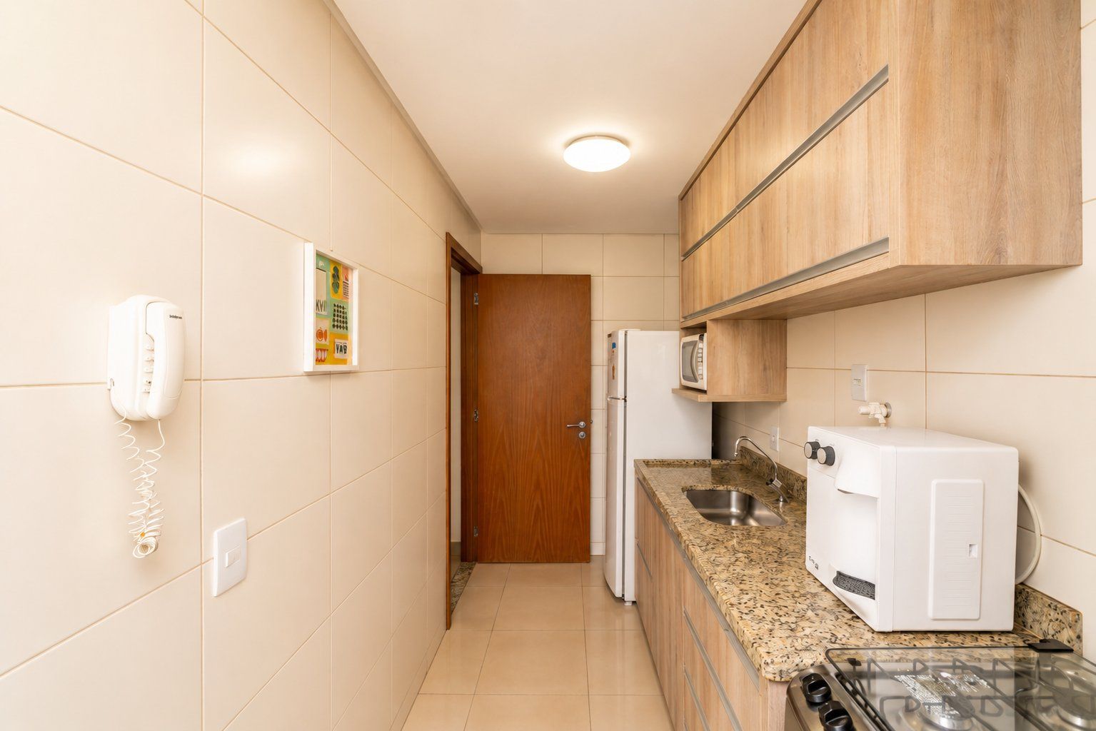 A kitchen with a refrigerator, microwave, stove, and a phone on the wall.