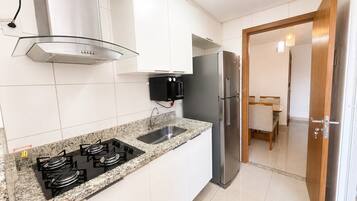 Una cocina moderna con armarios blancos, un refrigerador de acero inoxidable, una estufa a gas y un microondas integrado.