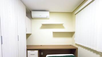 Una habitación pequeña y funcional con una cama individual, un escritorio y un equipo de aire acondicionado blanco instalado en la pared.