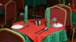 A dining table set with cutlery and glassware, surrounded by chairs with red and green patterned upholstery.