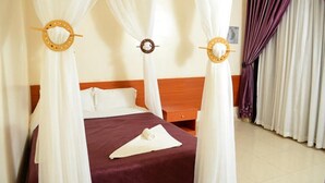 A hotel room with a bed, white curtains, and a wooden headboard.