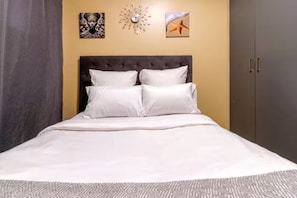 A bed with white bedding, a dark headboard, and a patterned rug. - Waterfall Hive (Midrand)