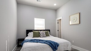 Un dormitorio con cama, mesita de noche, ventana y puerta.