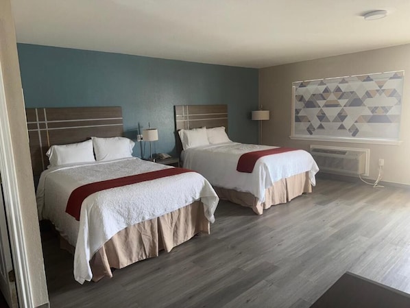 Una habitación de hotel con dos camas, una pared azul de acento, cortinas con diseño geométrico y suelo de madera.