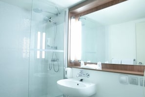 Un baño moderno con cabina de ducha de vidrio, un lavabo blanco y un espejo con marco de madera.
