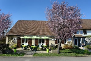 A building with a tiled roof, outdoor seating with tables and chairs, and flowering trees.