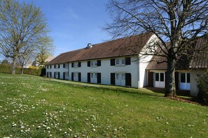 A two-story house with a sloped roof, a front lawn with scattered flowers, and a tree to the right.