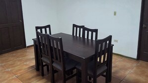 Ein Essbereich mit einem rechteckigen Tisch, vier Stühlen, einer Deckenleuchte und einem Fliesenboden.