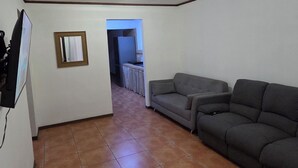 Ein Innenraum mit Fliesenboden, einem grauen Sofa und einem Fernseher links.