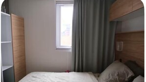 Un llit individual amb capçalera de fusta, una finestra amb cortines i un armari.
