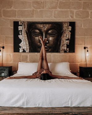Ein Bett, auf dem eine Person kopfüber liegt, eine Wand mit einem Buddha-Gemälde und zwei Nachttischlampen.