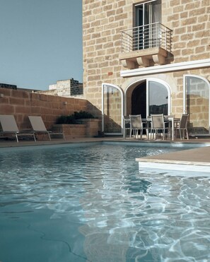 Ein Swimmingpool mit klarem Wasser, Liegestühlen und ein Steinhaus mit Balkon.