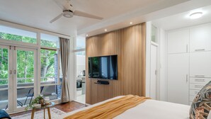 Moderni hotellihuone, jossa on suuri sänky, seinälle asennettu taulutelevisio, parveke, jossa on ruokailutila, sekä kattotuuletin.