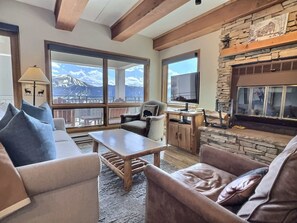 Ein Wohnzimmer mit Kamin, großen Fenstern und Bergblick.