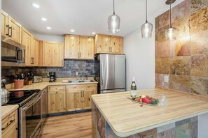 A modern kitchen with wooden cabinets, stainless steel appliances, a stone backsplash, and pendant lighting. - Private Hot Tub, Dog Friendly & Shuttle Access (Breckenridge)
