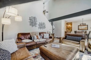 A modern living room with leather sofas, a coffee table, and a dining area with a chandelier. - Private Hot Tub, Dog Friendly & Shuttle Access (Breckenridge)