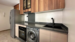 Una cocina compacta con refrigerador de acero inoxidable, horno integrado, lavadora y armarios de madera.