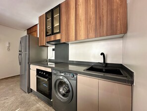 A compact kitchen with a stainless steel refrigerator, a built-in oven, a washing machine, and wooden cabinets. - Gauthier luxury studio (Casablanca)