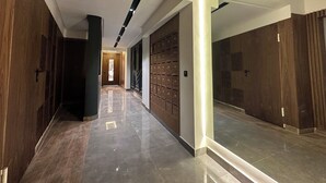 Un pasillo moderno con puertas de madera, suelo de baldosas e iluminación empotrada en el techo.