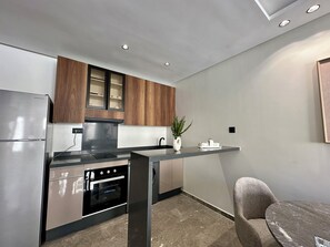 A modern kitchen with a built-in oven, stainless steel refrigerator, wooden cabinets, and a marble countertop. - Gauthier luxury studio (Casablanca)