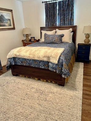 Une chambre à coucher avec un grand lit, deux tables de chevet, une fenêtre avec des rideaux et un tableau encadré au mur.