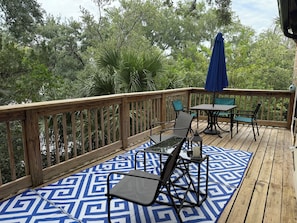 Eine Holzterrasse mit Gartenmöbeln, darunter Stühle und ein Tisch, und einem blauen Teppich mit Muster.