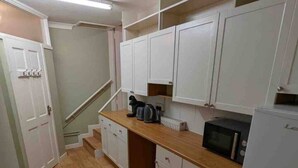 A compact kitchen with white cabinets, a microwave, a kettle, and a radiator.