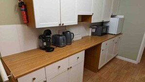 A compact kitchen with white cabinets, a wooden countertop, and a coffee maker.