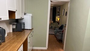 A narrow hallway leading to a bedroom with a bed, a bedside table, and a lamp.
