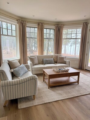 Ein Wohnzimmer mit einem gestreiften Sofa, einem Holztisch und großen Fenstern mit Vorhängen.