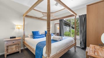 A four-poster canopy bed with a view of the outdoors, a bedside table, and a wooden wardrobe.