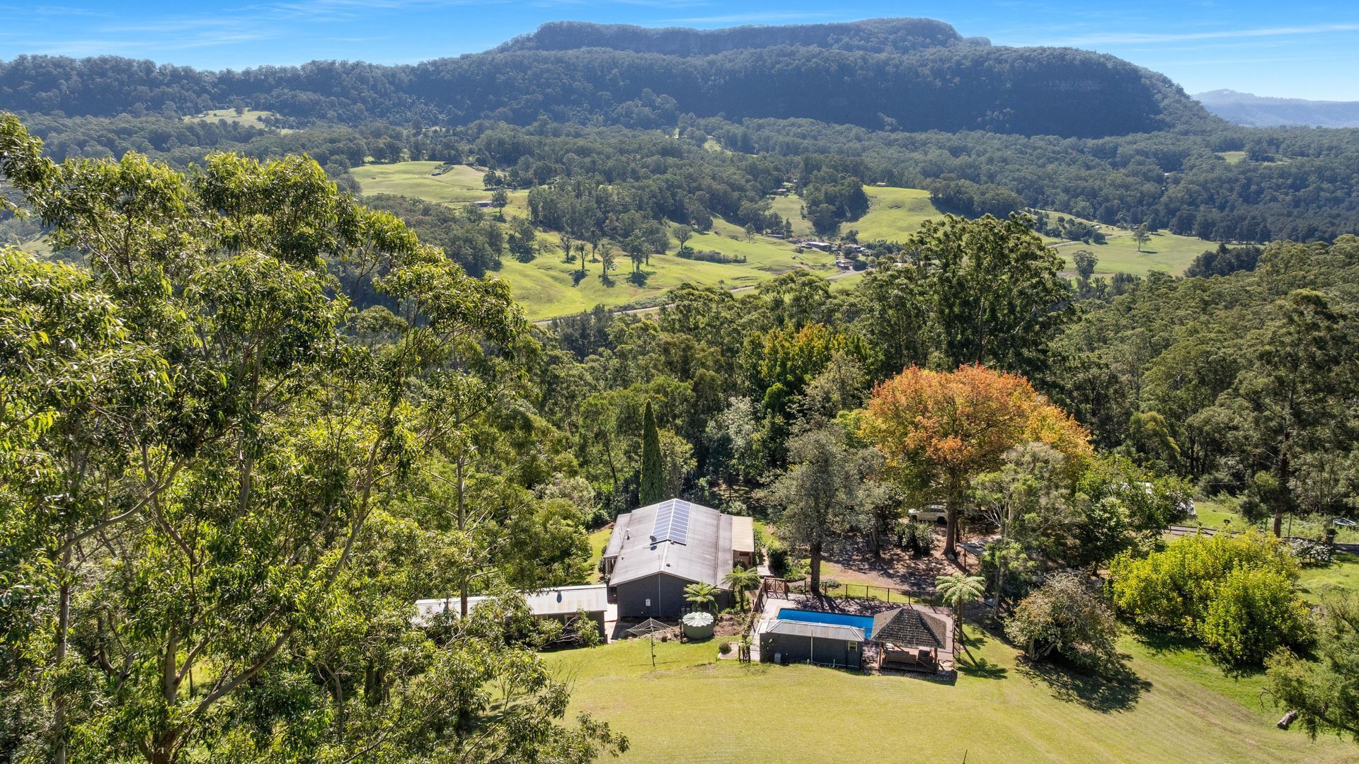 A rural property with a large barn, open fields, and dense forest.