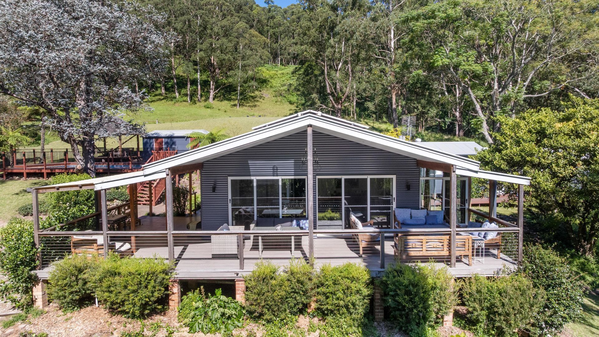 A modern house with a large deck, a covered patio, and a view of the surrounding forest.