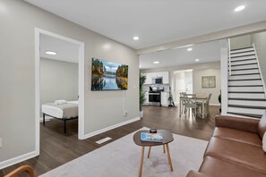 Una sala de estar moderna con sofá, una mesa de centro, un cuadro y una escalera que conduce a un comedor.
