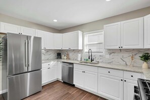Una cocina moderna con armarios blancos, electrodomésticos de acero inoxidable, salpicadero de mármol y suelo de madera.