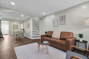 Una sala de estar moderna con un sofá de cuero marrón, una mesa redonda de centro y una escalera que lleva a otra habitación.