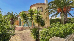 A building with a tiled roof, a stone pathway, and palm trees. - Villa Flamingo. Private swimming pool. Ideal for families. (Les Tres Cales)