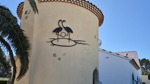 A building with a circular structure, a decorative bird mural, and a stone pathway. - Villa Flamingo. Private swimming pool. Ideal for families. (Les Tres Cales)