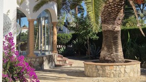 A courtyard with palm trees, a white building with arches, and a stone pathway. - Villa Flamingo. Private swimming pool. Ideal for families. (Les Tres Cales)