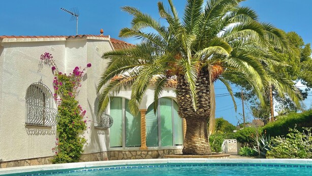 A pool with a palm tree, a building with a stone facade, and a window with a metal grille. - Villa Flamingo. Private swimming pool. Ideal for families. (Les Tres Cales)