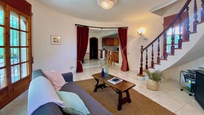 A living room with a sofa, a coffee table, a staircase, and a view into the kitchen. - Villa Flamingo. Private swimming pool. Ideal for families. (Les Tres Cales)
