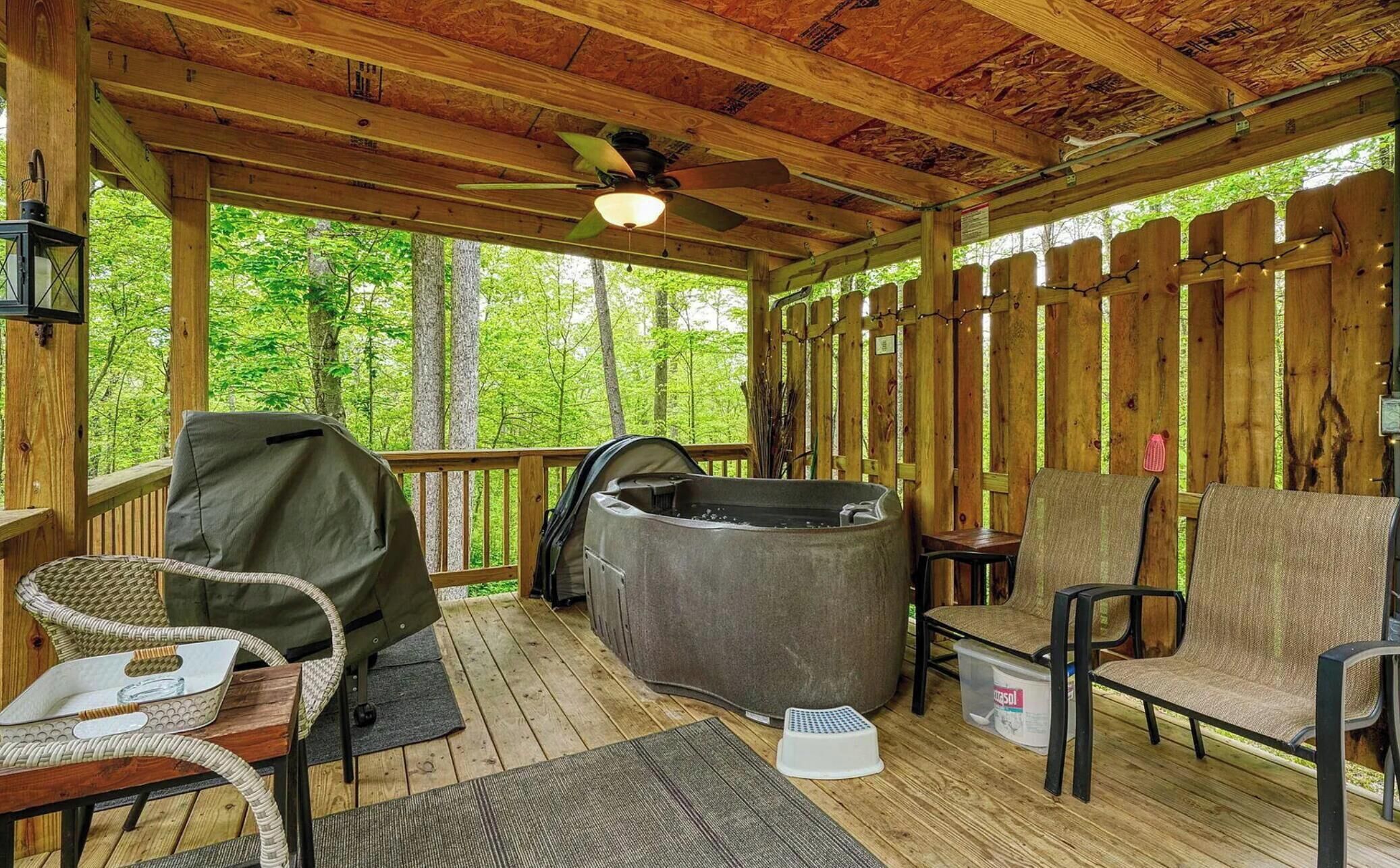 Terraza techada al aire libre con mobiliario de madera, un jacuzzi y un ventilador de techo.