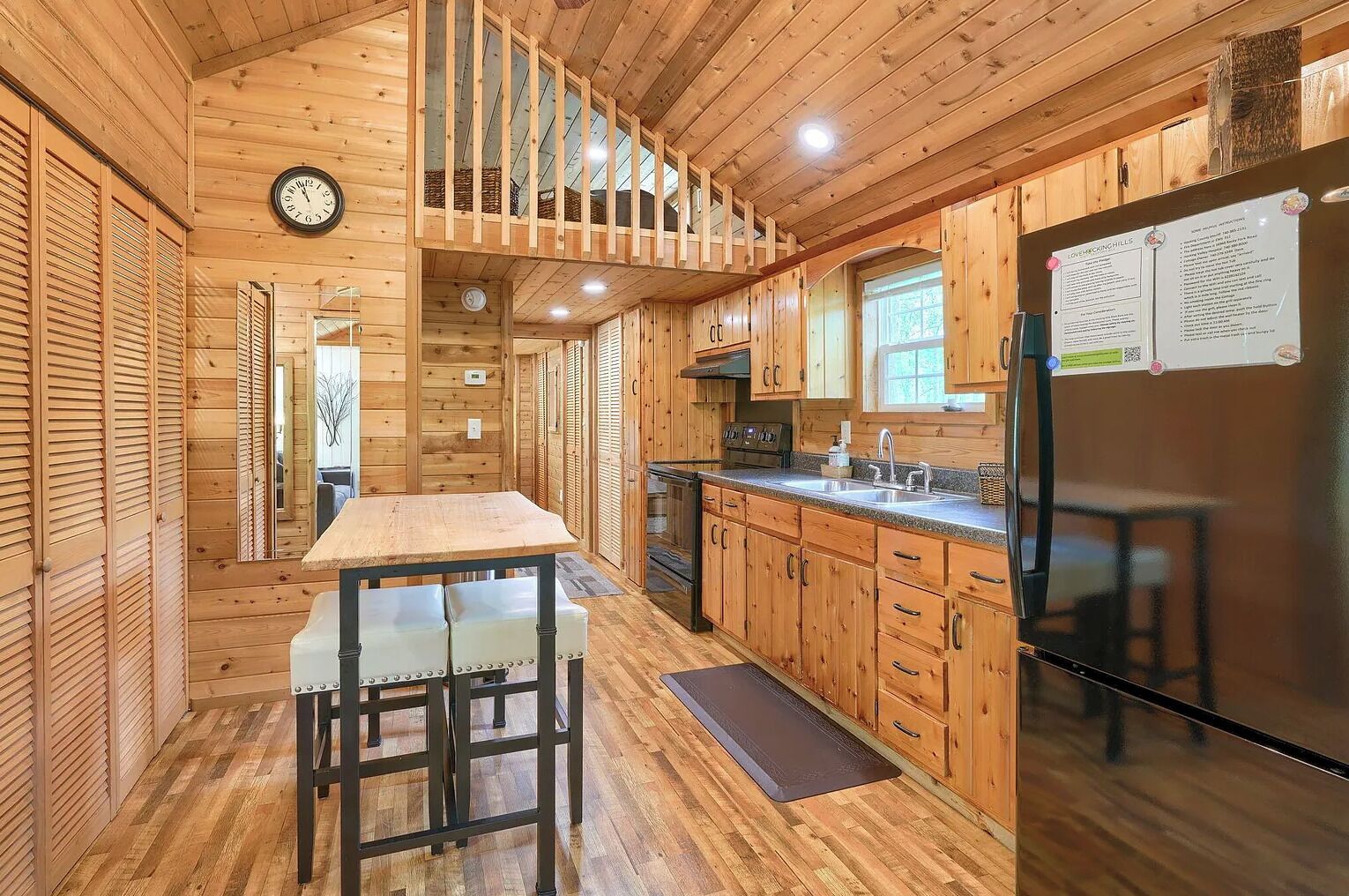 A wooden cabin interior with a kitchen area, including a dining table, chairs, and a refrigerator.