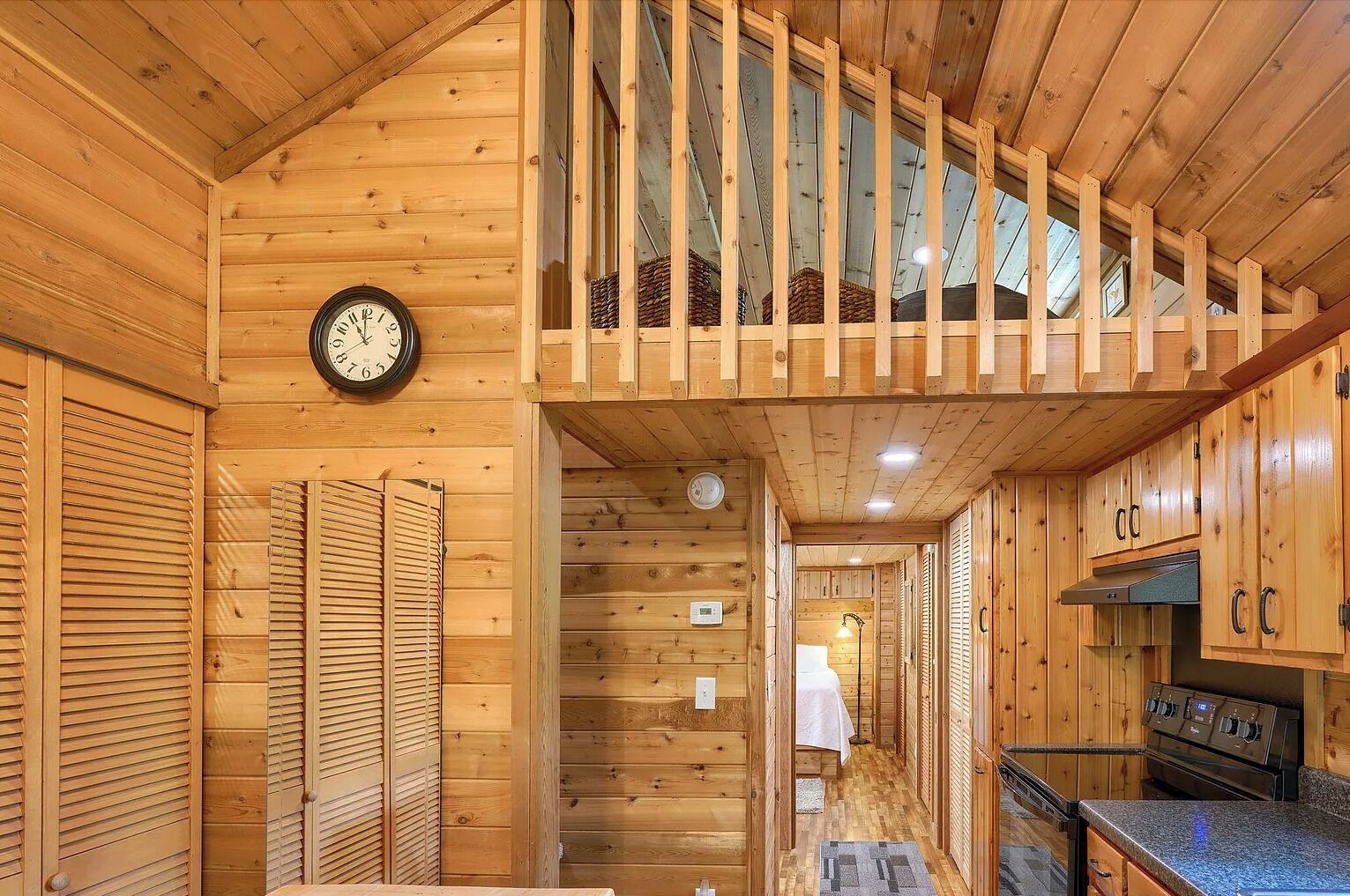 A wooden cabin interior with a kitchen, a dining area, and a staircase leading to a loft.
