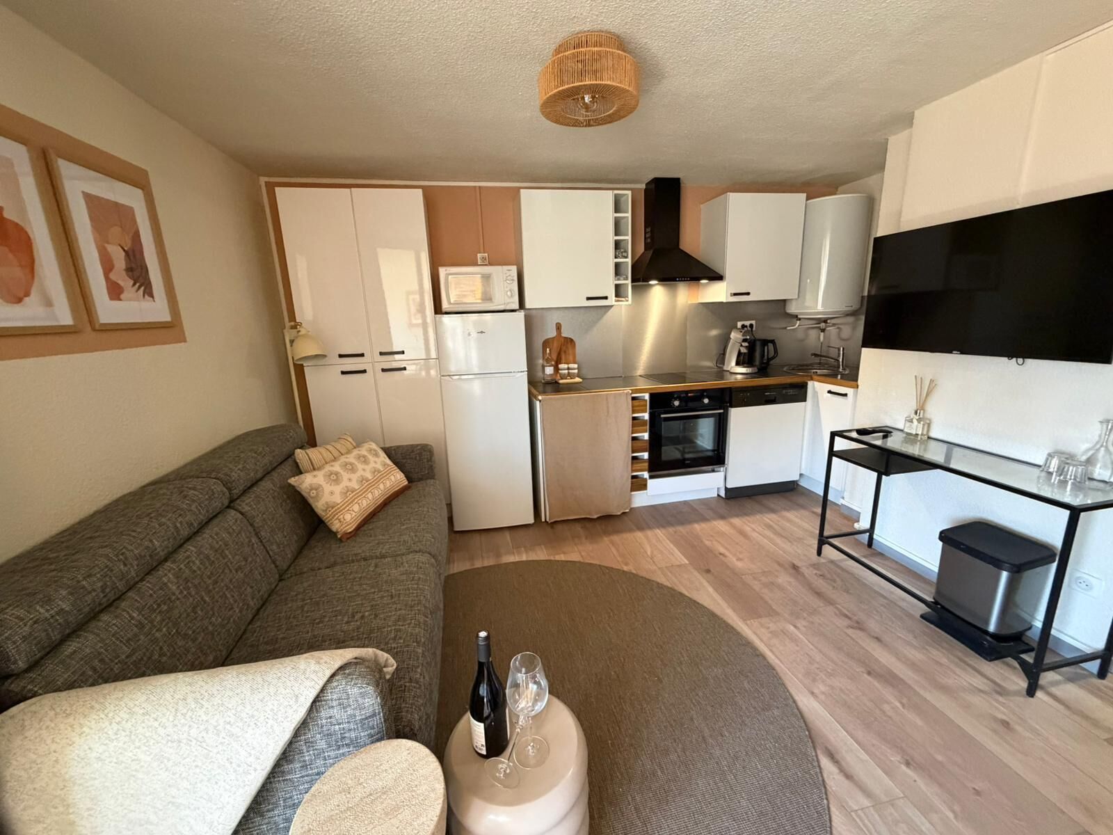 Un espacio habitable compacto con un sofá, una pequeña mesa de centro, una zona de cocina que incluye microondas, horno y un televisor.
