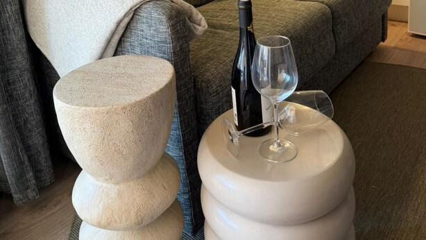 A living room with a sofa, a round table with a bottle and glass, a stone sculpture, and two framed artworks on the wall. - Modern Beach Apartment Valras (Valras-Plage)