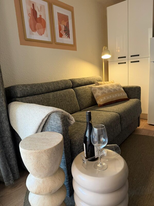Ein Wohnzimmer mit einer Couch, einem runden Tisch mit Flasche und Glas, einer Steinskulptur sowie zwei gerahmten Kunstwerken an der Wand.