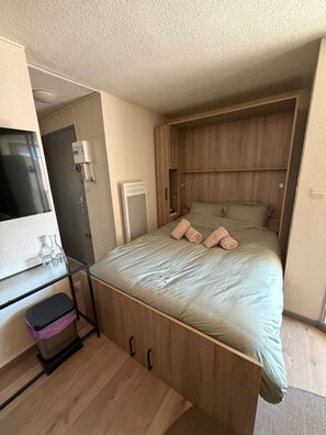Ein kleines Zimmer mit einem Bett, einem Schreibtisch, einem Fernseher und einem Kleiderschrank.