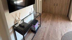 A living room with a flat-screen TV mounted on a wall, a glass coffee table with a remote control, a small vase, and a storage box. - Modern Beach Apartment Valras (Valras-Plage)